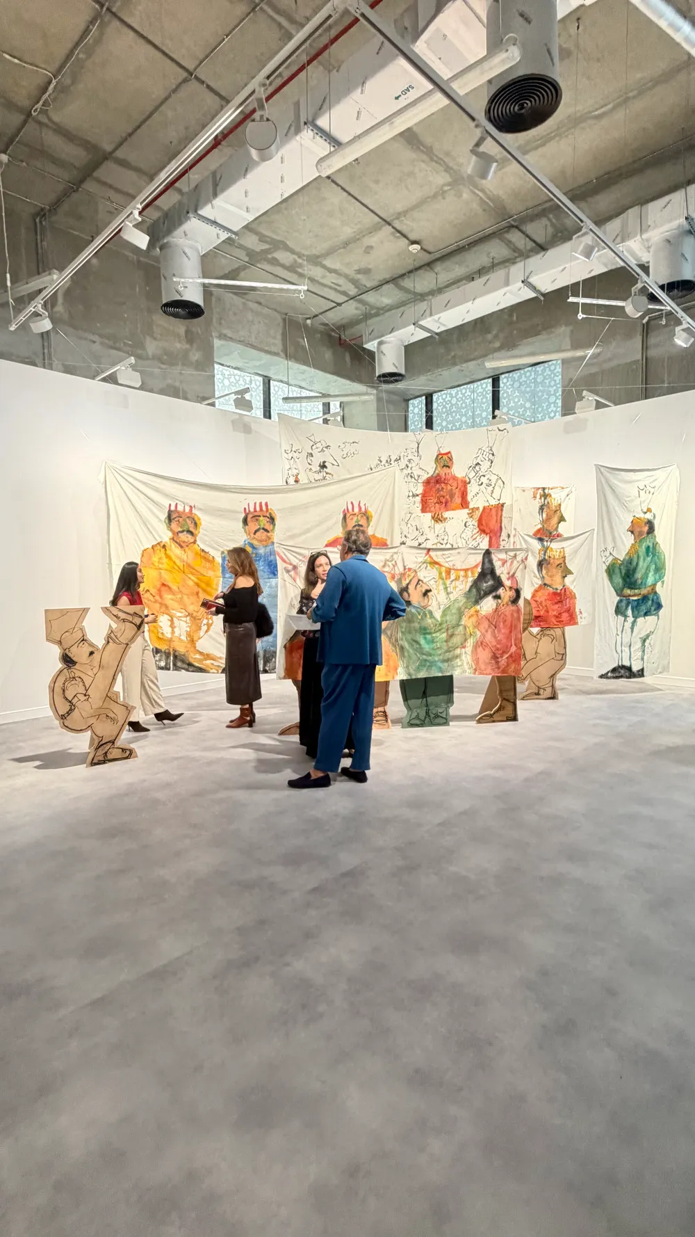 Art Basel Katar’da Aiza Ahmed’e ait, figüratif çizimlerin kumaş yüzeyler ve kesit formlar üzerinden mekâna yayıldığı yerleştirme çalışması ve izleyiciler.