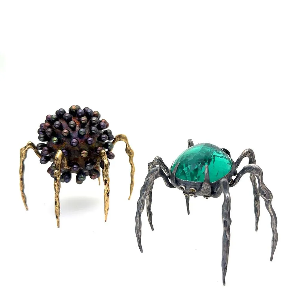 Farklı taş ve metal yüzeylerle tasarlanmış iki heykel formu, örümceği çağrıştıran ayak yapısıyla yan yana konumlanmış.