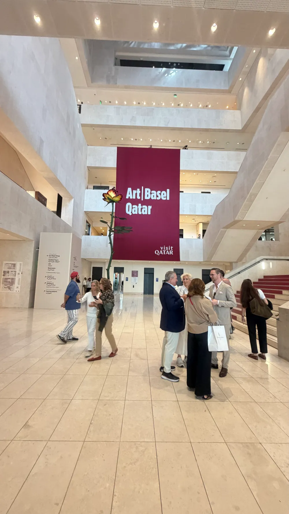 Art Basel Katar’da Pilot Galeri alanından bir genel görünümde, merkezde Art Basel Qatar afişi ve fuaye alanında ziyaretçiler yer alıyor.