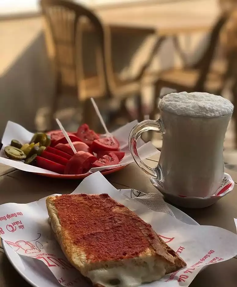 Şeflerin lezzet rotaları listesinde yer alan yol üstü duraklarından biri olan Düzdağ Tost'tan, kıtır ekmeği, erimiş peyniri ve özel salçasıyla ünlü Susurluk tostu, yanında köpüklü ayran, domates ve turşu tabağıyla iştah açıcı bir sunumla masada duruyor.