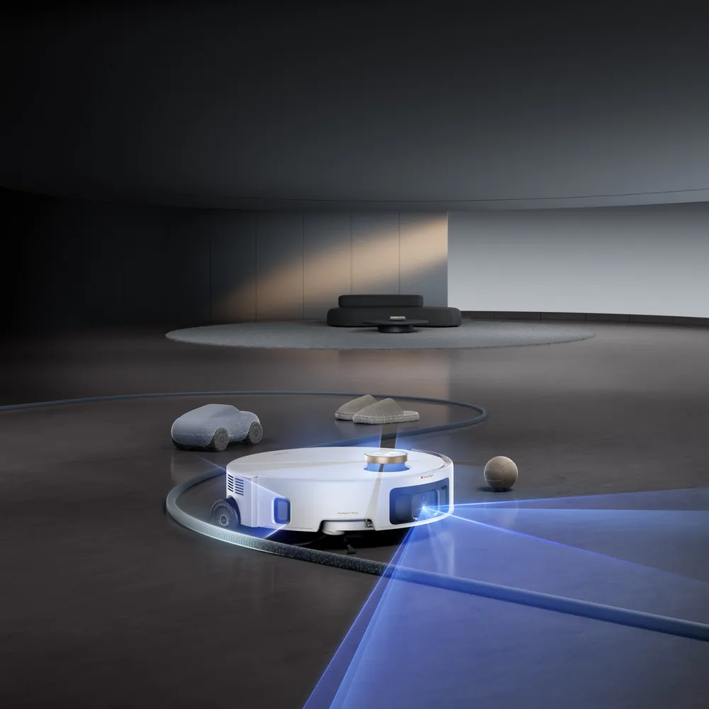 Beyaz renkli, lazer navigasyon ışınları yayan bir robot süpürge, modern ve minimalist bir odanın koyu zemininde, önündeki terlik, oyuncak araba ve top gibi engellerin etrafından zekice dolaşarak evi temizliyor ve koltuk altına girebilen akıllı robot süpürgelerin evin her köşesini nasıl temizlediğini vurguluyor.