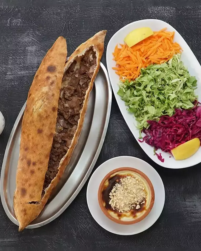 Uzunlamasına kesilmiş, bol etle dolu bir pide, oval metal tepside sunulurken yanında rendelenmiş havuç, marul ve kırmızı lahana içeren taze bir salata ile limon dilimleri, ve üstü öğütülmüş fındıkla süslenmiş bir kase sütlaç; bu sofra, Duru Akgül'ün şeflerin lezzet rotaları listesinde İstanbul Tepeüstü'ndeki favori lezzet kaçamağı olarak belirttiği Lider Pide'nin zenginliğini yansıtıyor.