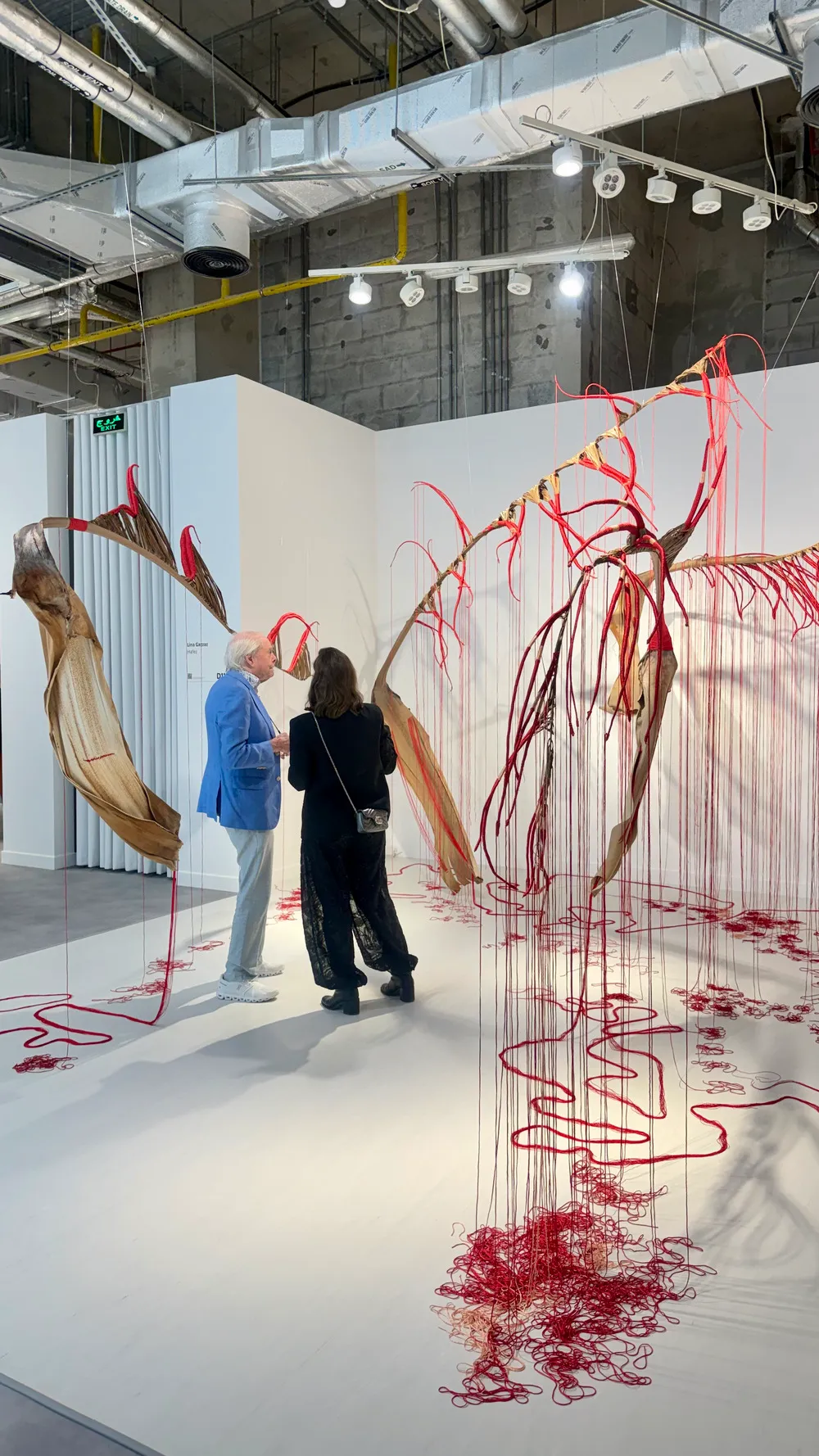 Art Basel Katar’da Lina Hazzaz’a ait kırmızı iplerle kurgulanmış, organik formların mekân içinde yayıldığı yerleştirme çalışması önünde izleyiciler yer alıyor.