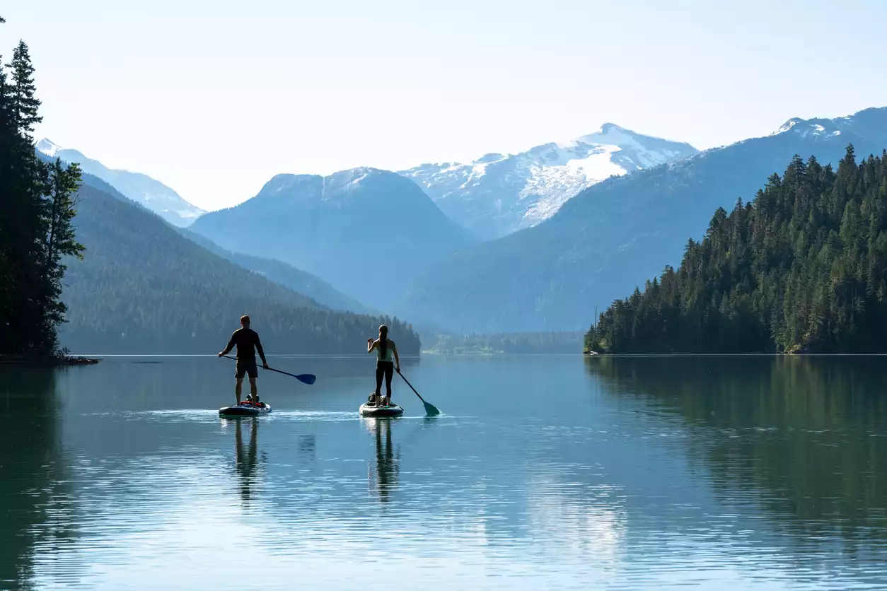 Gölde dağ manzarasına karşı paddle board yapan çift