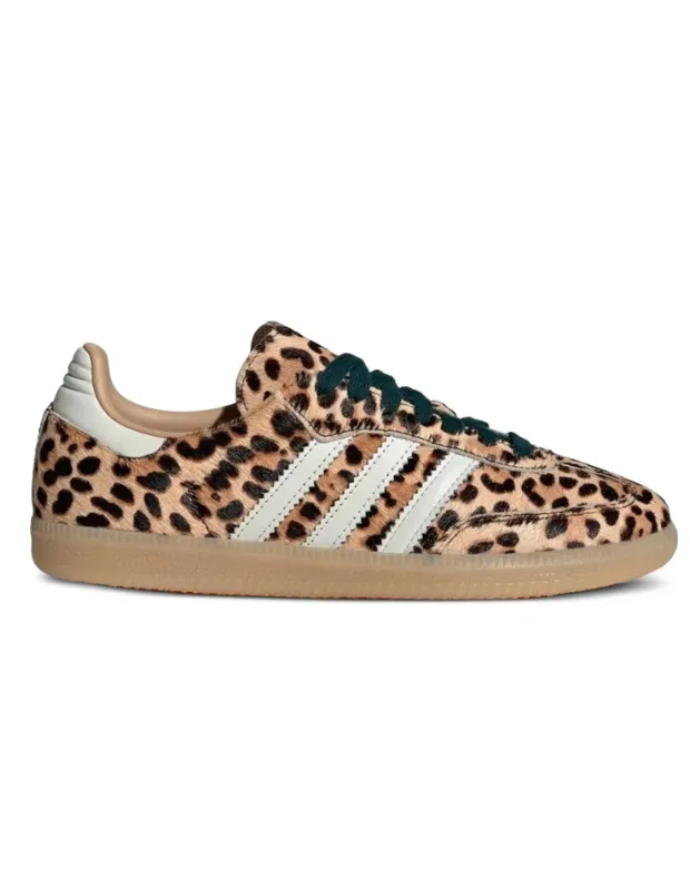 Leopar desenli tüylü yüzeye sahip, beyaz üç çizgili ve koyu yeşil bağcıklı, kahverengi tabanlı tek bir Adidas Samba spor ayakkabı, beyaz bir arka plan üzerinde yan görünümüyle sergileniyor.