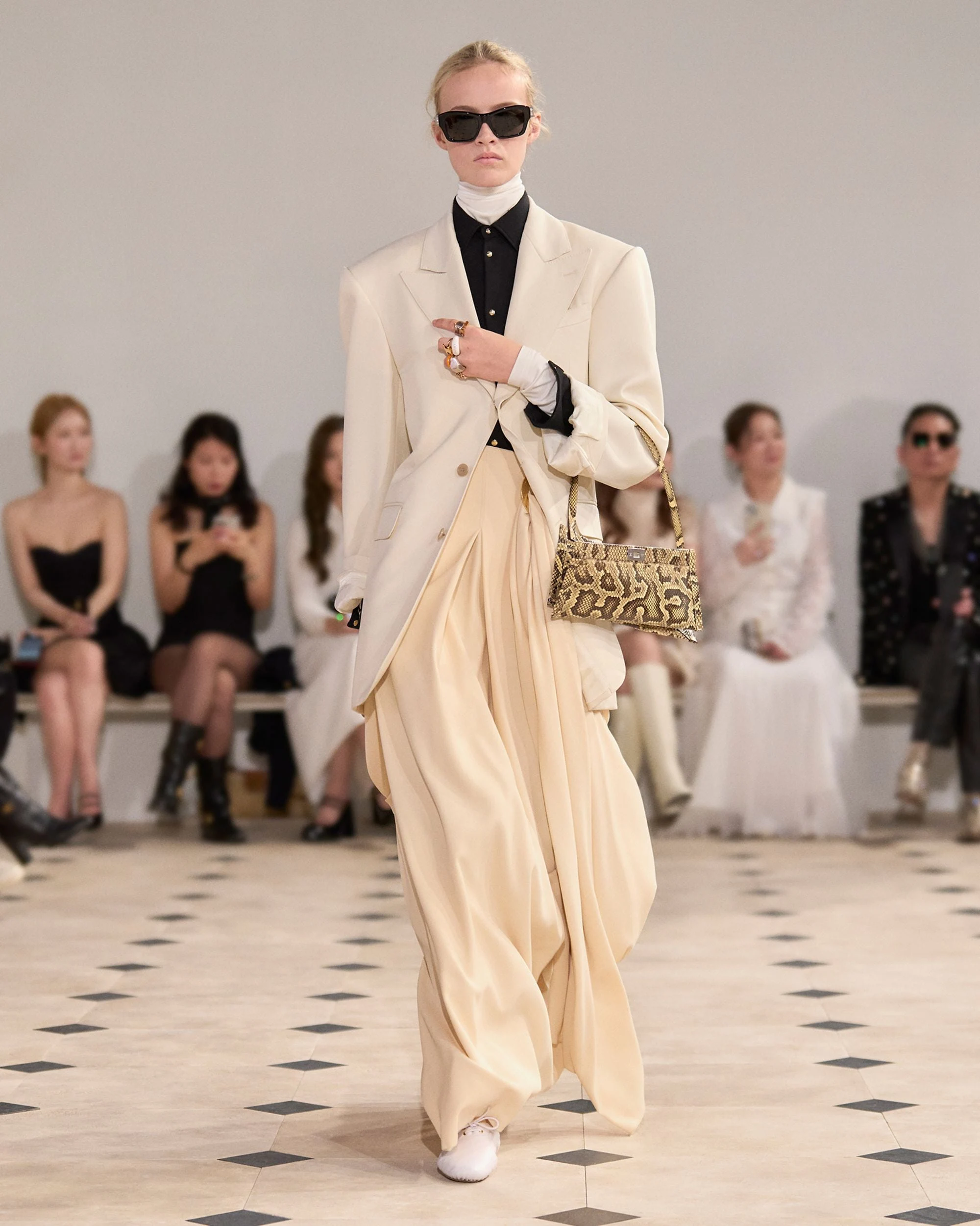 Celine İlkbahar-Yaz 2025 defilesinde model, krem oversize blazer, akışkan wide leg pantolon ve yılan desenli çanta ile modern tailoring ve zarif silueti yansıtan güçlü bir runway görünümü sergiliyor.