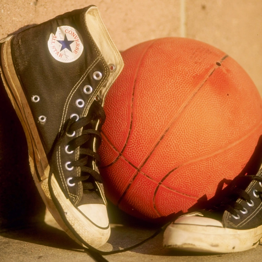 Basketbol topu yanında duran siyah Converse Chuck Taylor spor ayakkabılar, retro tonlu ışıkla çekilmiş sokak stili detay görüntüsü.
