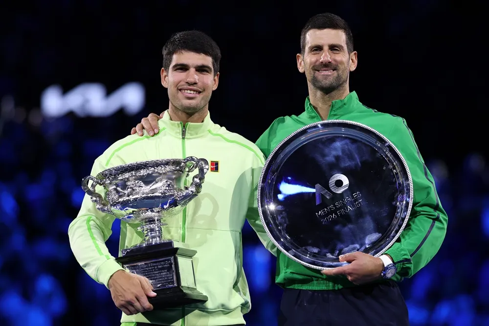 Carlos Alcaraz, 2026 Avustralya Açık finali sonrası Novak Djokovic ile birlikte kupa töreninde poz verirken.