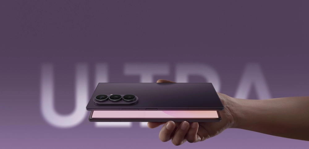 Mor bir arka plan üzerinde, elinde kısmen açık tutulan mor renkli bir Galaxy Z Fold8 Ultra katlanabilir telefonun üçlü kamera modülü ve iç ekranının ucu görünüyor, telefonun arkasındaki bulanık ULTRA yazısı ise dikkat çekiyor.