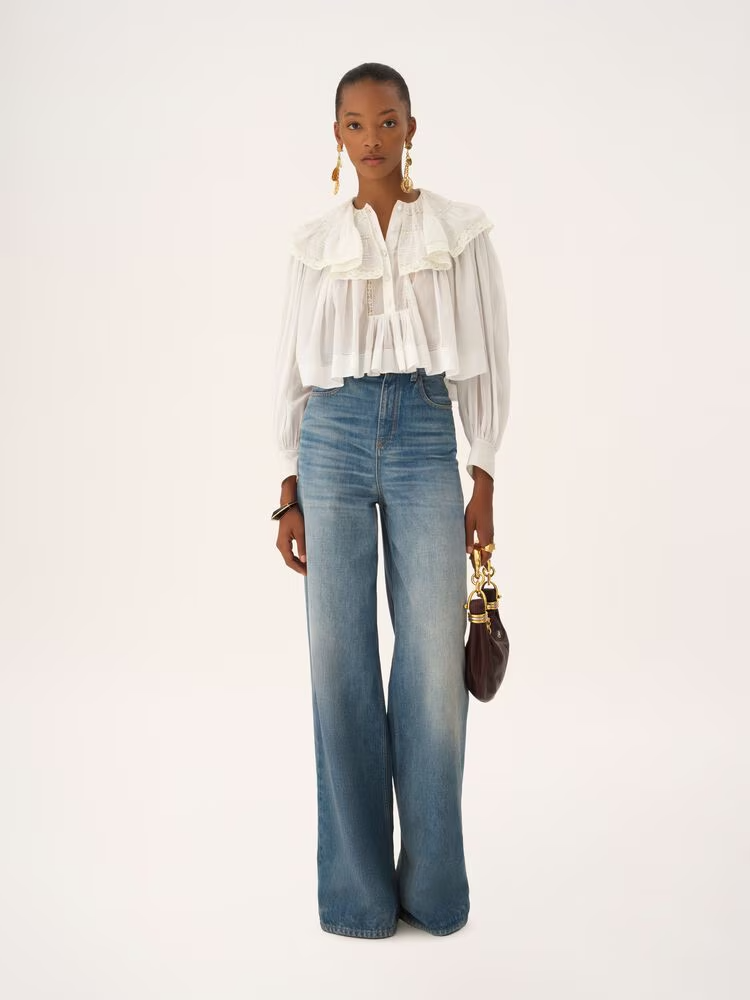 Yüksek bel wide leg jean pantolon ve romantik fırfırlı beyaz bluz kombini; modern kadın stilinde dengeli oranlar ve zamansız denim silueti.