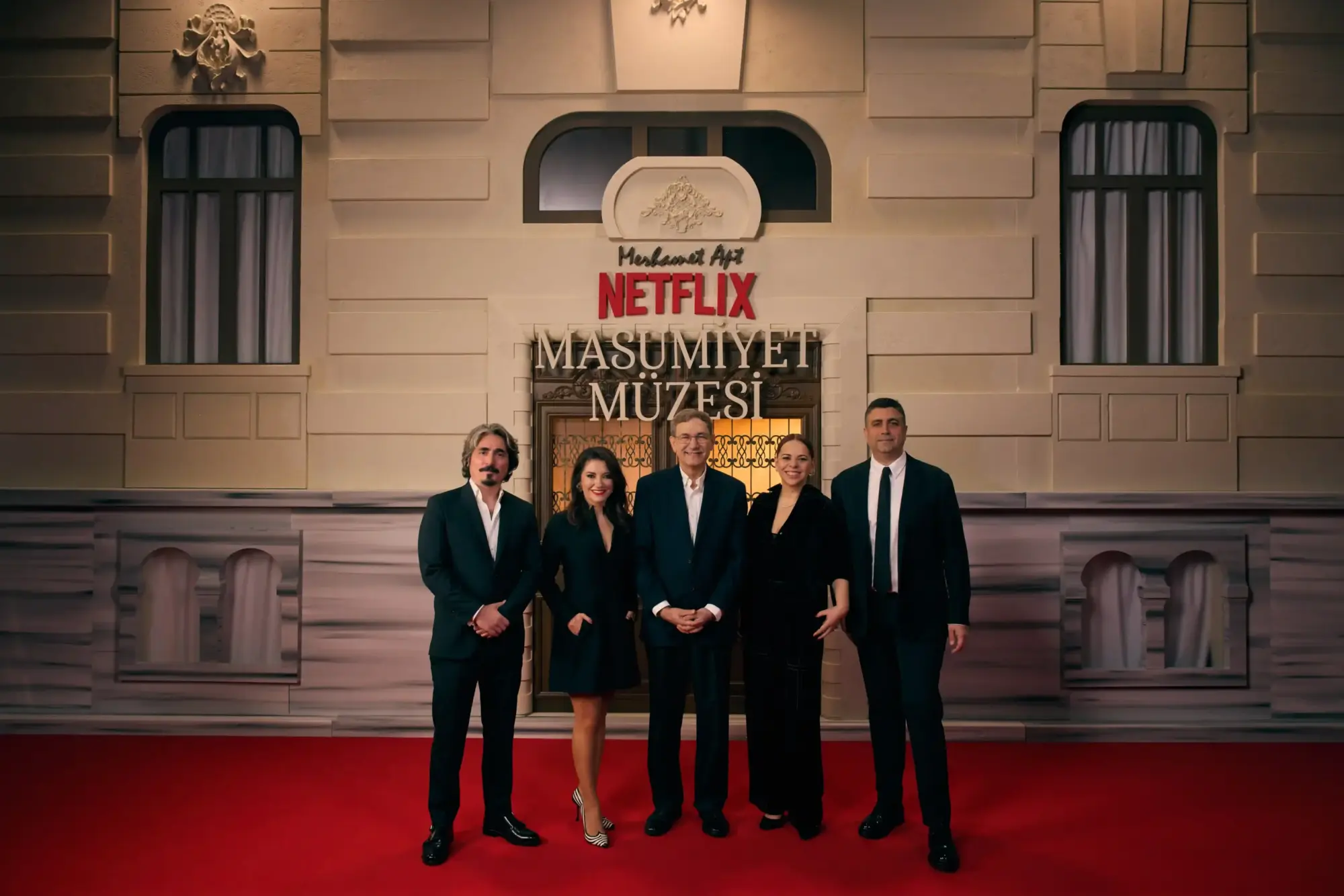 Netflix “Masumiyet Müzesi” galasında kırmızı halıda poz veren Ertan Kurtulan, Özge Bağdatlıoğlu, Orhan Pamuk, Zeynep Günay, Kerem Çatay; arkada dizi logosu ve tarihi bina cephesi.