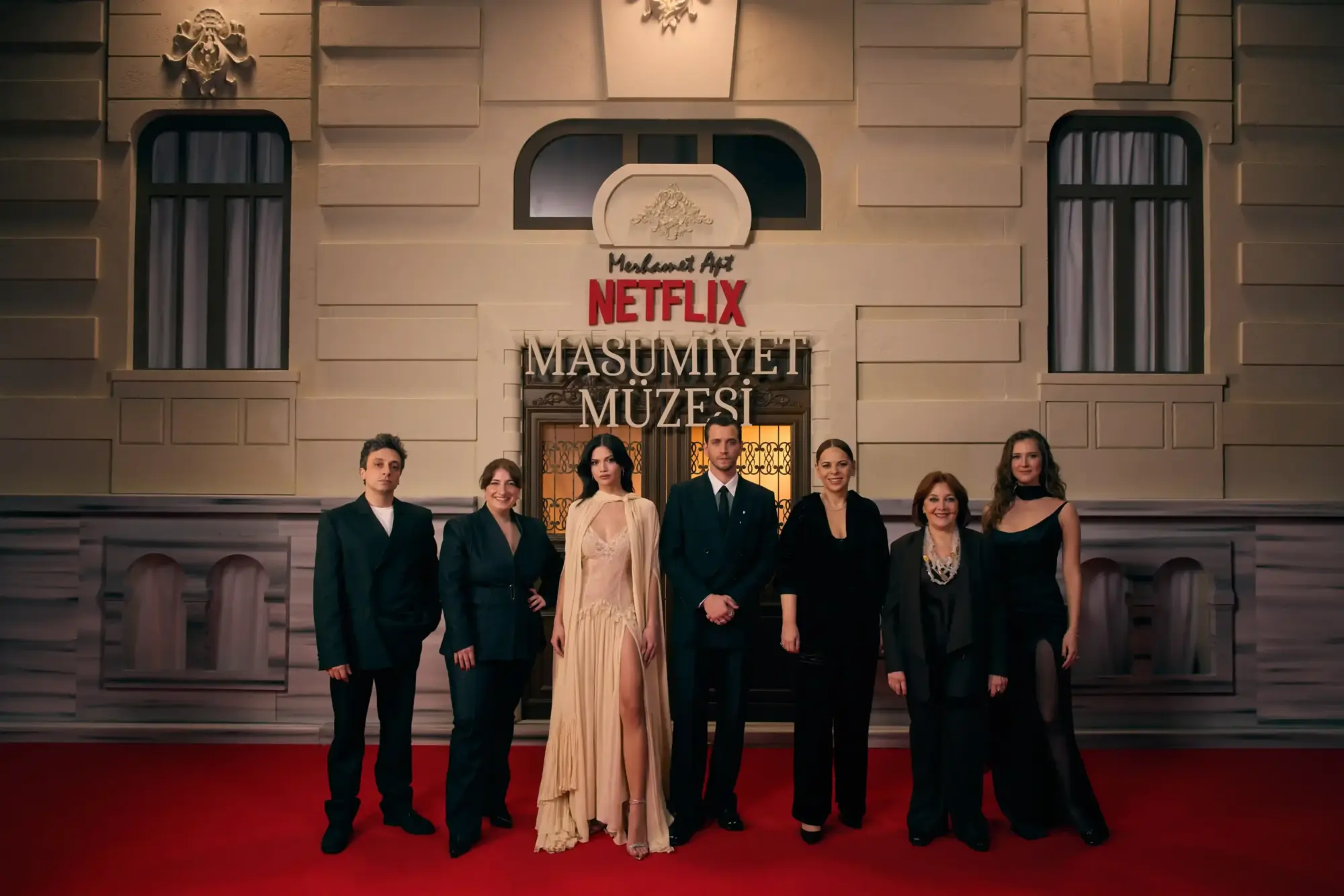 Netflix “Masumiyet Müzesi” galasında kırmızı halıda birlikte poz veren Onur Ünsal, Gülçin Kültür Şahin, Eylül Lize Kandemir, Selahattin Paşalı, Zeynep Günay, Tilbe Saran, Oya Unustası; arkada dizi logosu ve tarihi bina cephesi.