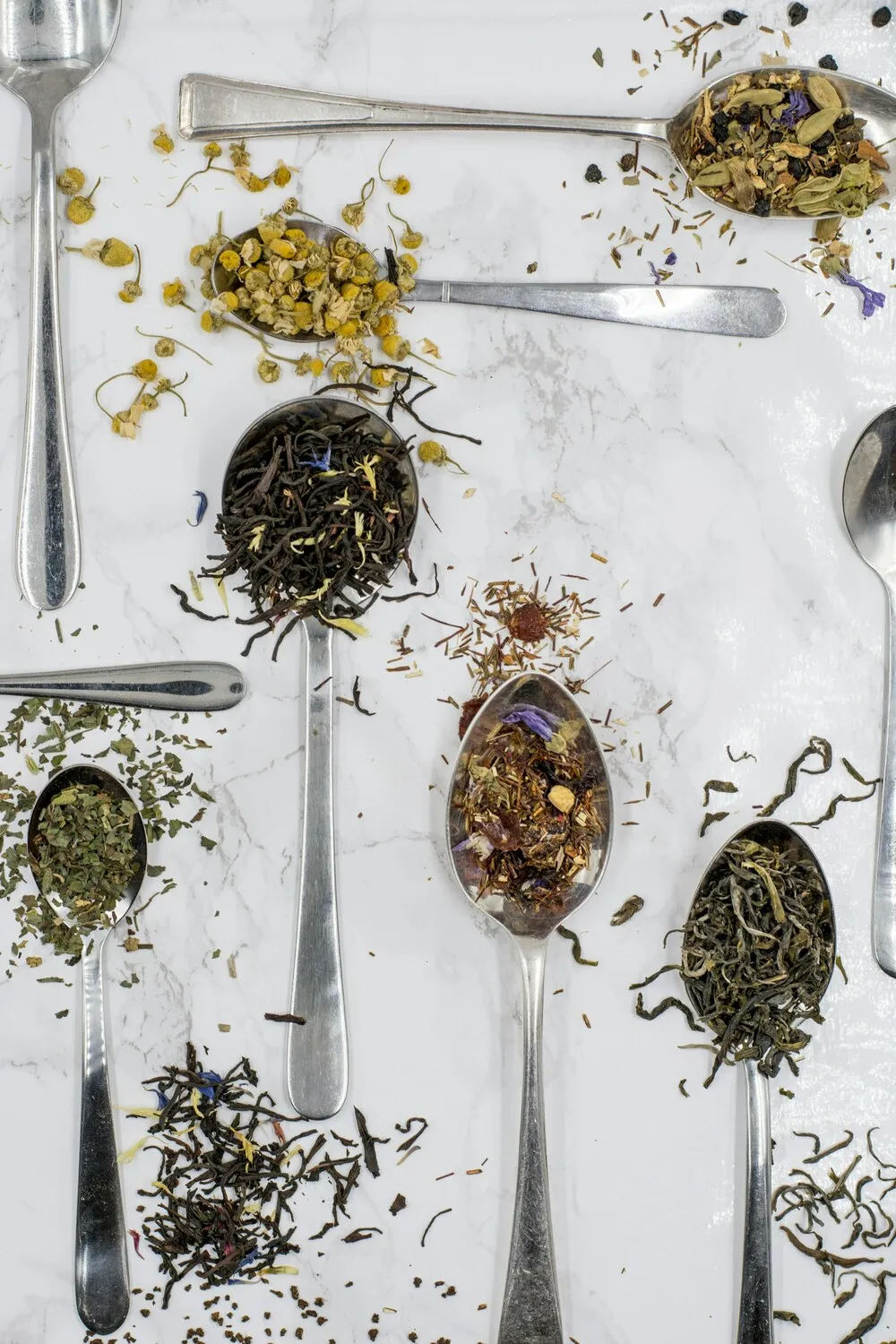 Farklı kurutulmuş bitkiler ve çay karışımları metal kaşıklar içinde; menopoz sürecinde bitkisel destekleri temsil eden görsel.