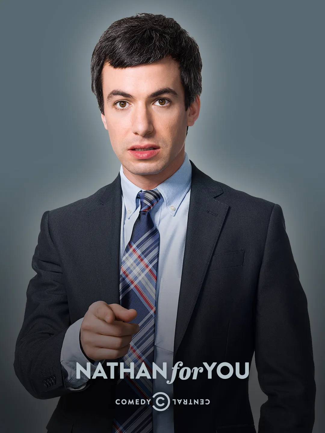 Nathan Fielder takım elbiseyle kameraya işaret ederken gri arka planlı tanıtım görselinde yer alıyor.