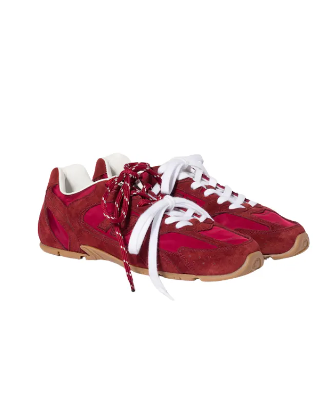 New Balance ve Miu Miu iş birliğinin dikkat çeken bir parçası olan, süet ve kumaş detaylı, koyu kırmızı renkli bu spor ayakkabılar, biri beyaz diğeri bordo-beyaz benekli bağcıkları ve açık kahverengi tabanlarıyla beyaz zeminde konumlandırılmış.