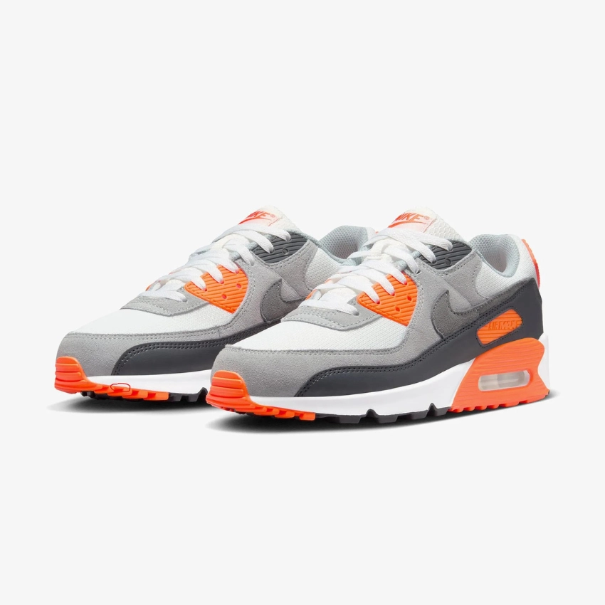 Gri, beyaz ve turuncu detaylara sahip Nike Air Max 90 spor ayakkabı modeli, beyaz fonda yan açıdan ürün çekimi.