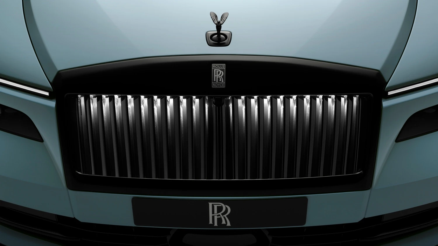 Rolls-Royce Spectre Series 2 Black Badge elektrikli lüks otomobilin mavi ön tasarımını gösteren bu detaylı görselde, ışıklı dikey ızgara çubuklarına sahip parlak siyah ön ızgara ve kaputun üzerinde siyah Spirit of Ecstasy figürü dikkat çekiyor.