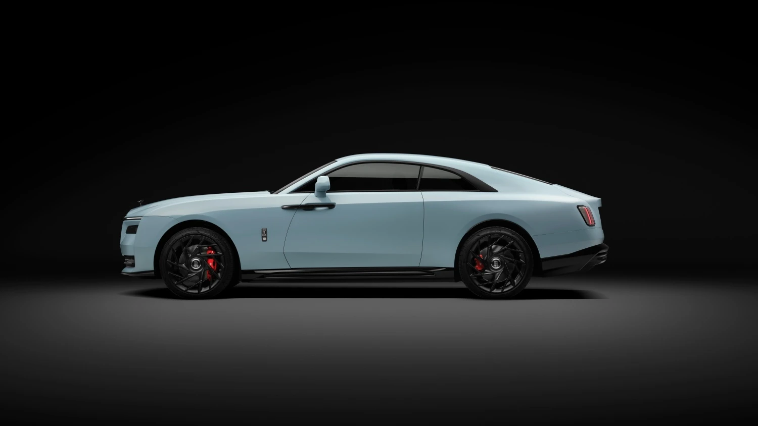 Koyu, minimalist bir arka plan önünde konumlandırılmış, açık mint yeşili renkteki elektrikli Rolls-Royce Spectre Black Badge modelinin zarif yandan görünümü; kırmızı fren kaliperlerine sahip parlak siyah çok kollu jantlarıyla güncellenmiş tasarımının getirdiği modern ve lüks çizgileri gözler önüne seriyor.