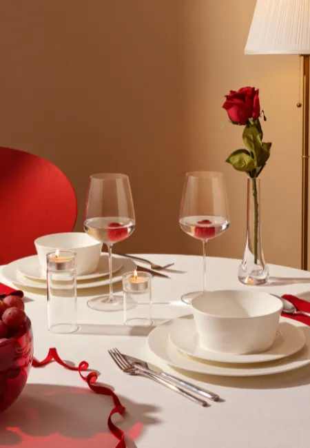 Romantik akşam yemeği için hazırlanmış masa: beyaz masa örtüsü, kırmızı gül, mumlar, şarap kadehleri ve şık sofra düzeni.