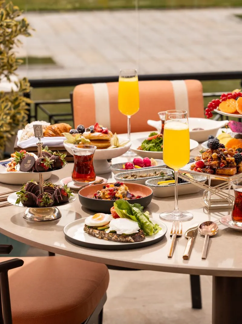 Çırağan'ın açık hava terasında, çikolatalı çilekler, meyveli pankekler, kruvasanlar, poşe yumurtalı avokado tostları, Türk çayı ve mimosalarla dolu, zengin çeşitlilikte lüks bir brunch masası sergileniyor.