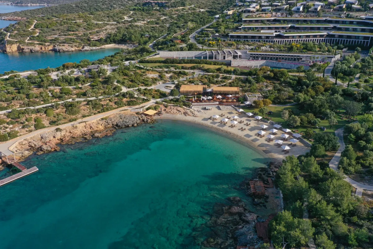 Havadan çekilmiş bu geniş açılı fotoğrafta, Ege Denizi'nin berrak turkuaz sularıyla çevrili, yeşil tepelerin yamacına kurulmuş Six Senses Kaplankaya tesisi, şemsiyeler ve şezlonglarla dolu özel kumlu plajı ve modern yapılarıyla göz alıyor.