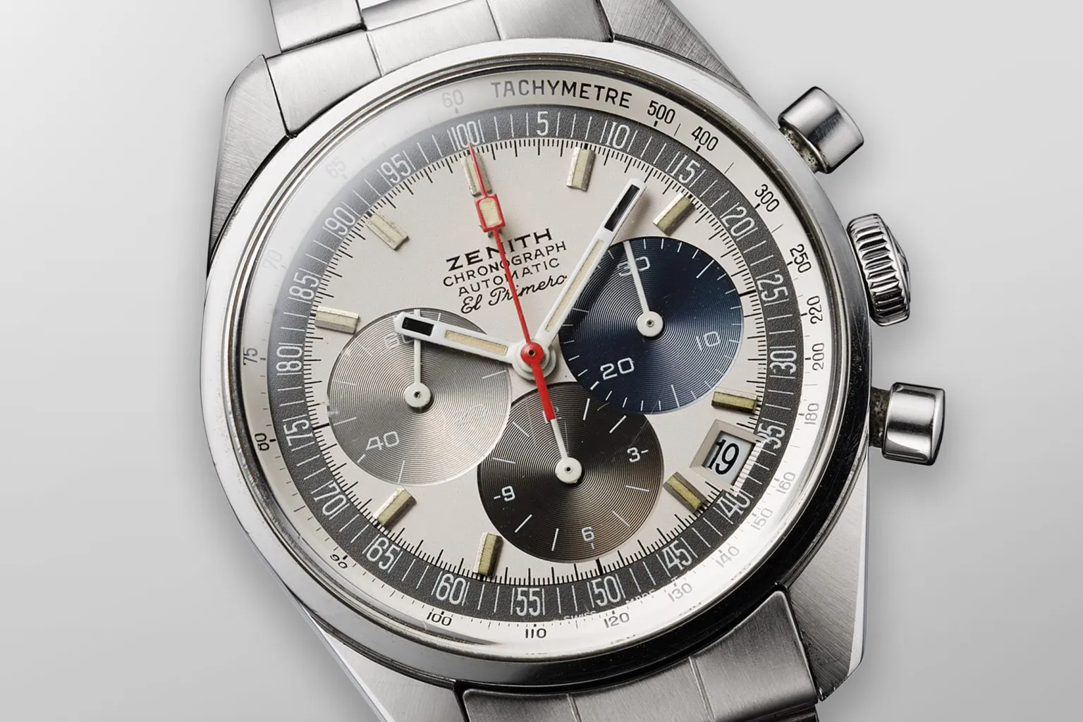 Gümüşi-beyaz kadranı, kendine özgü üç renkli alt kadranları (iki gri, biri lacivert tonlarında), kırmızı kronograf ibresi ve takimetre ölçeğiyle Zenith El Primero, 1969 yılında dünyanın ilk yüksek frekanslı otomatik kronografı olarak saat tarihini değiştiren ikonik bir modelin yakın çekimini gösteriyor.