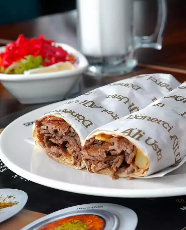 Oggusto, Salvatore Cannetiello – Şeflerin Lezzet Rotaları. Beyaz tabakta sunulan, üzerinde 'Dönerci Ali Usta' yazılı iki parça et döner dürüm. Şefin vazgeçilmez lezzet durağı olan bu menüye arka planda kırmızı lahana salatası ve köpüklü bir bardak ayran eşlik ediyor.