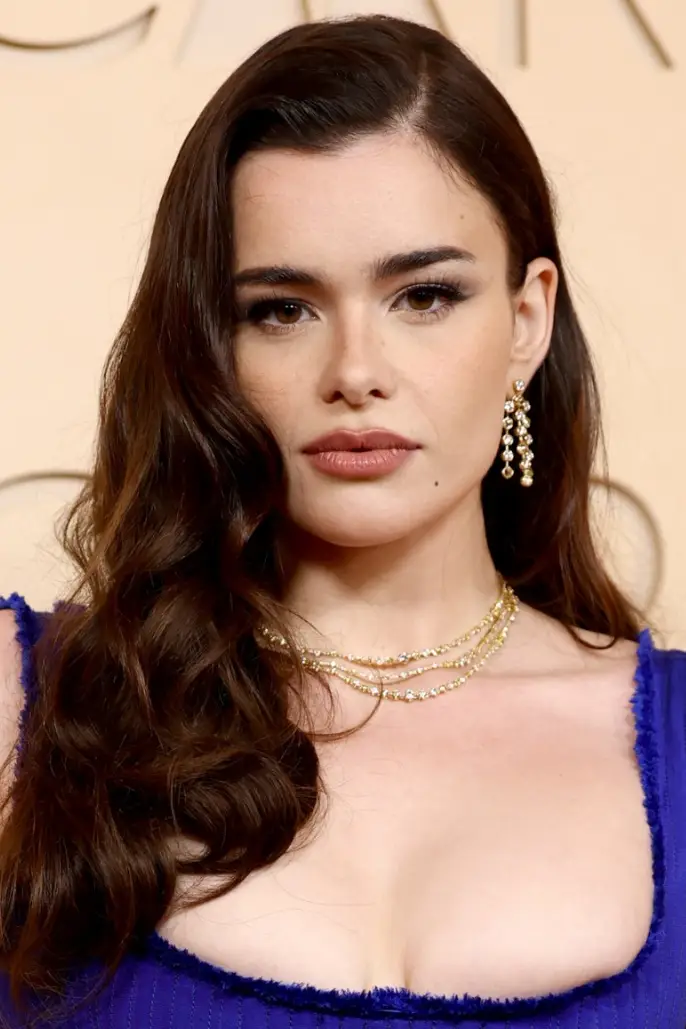 Barbie Ferreira, dalgalı koyu kahve saçları, dikkat çekici göz makyajı ve pembe dudaklarıyla doğrudan kameraya bakarken, derin yakalı parlak mavi elbisesini ve zarif pırlanta kolye ile küpelerini sergiliyor, bu şık görünümüyle bir Oscar etkinliğinde olduğu izlenimi veriyor.