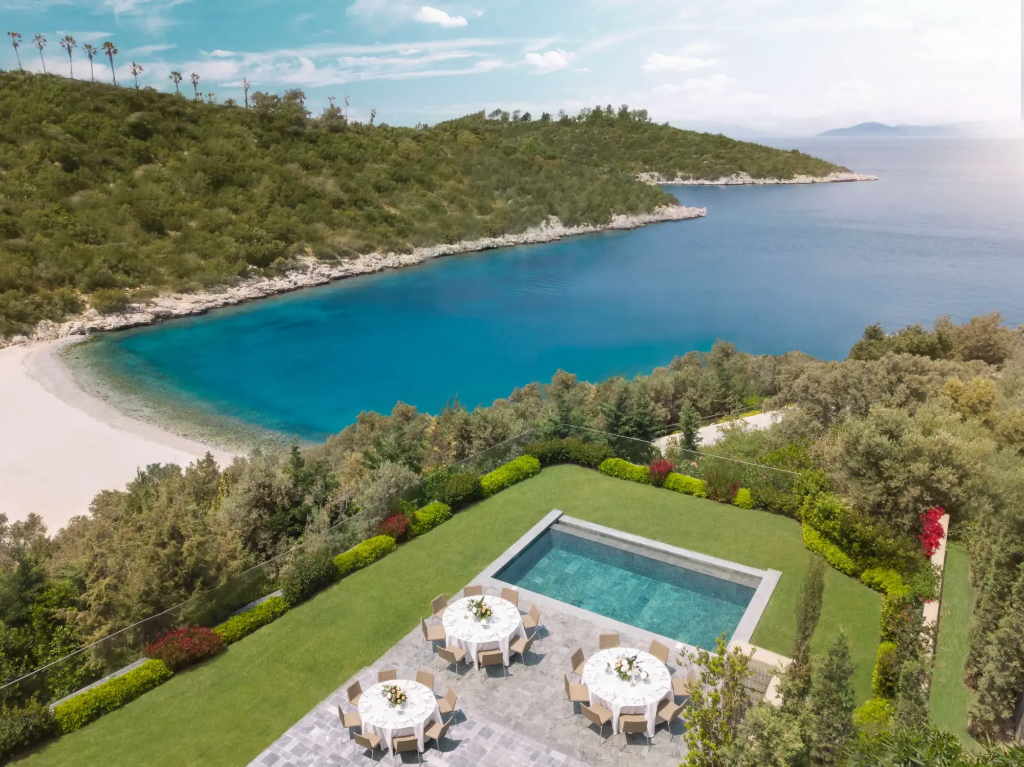 Yemyeşil tepelerle çevrili masmavi bir koyun üzerinde yer alan lüks bir Bodrum düğün mekânı, berrak havuzu ve çiçeklerle süslü zarif yuvarlak masalarıyla hazırlanmış çim alanıyla unutulmaz davetlere ev sahipliği yapıyor.