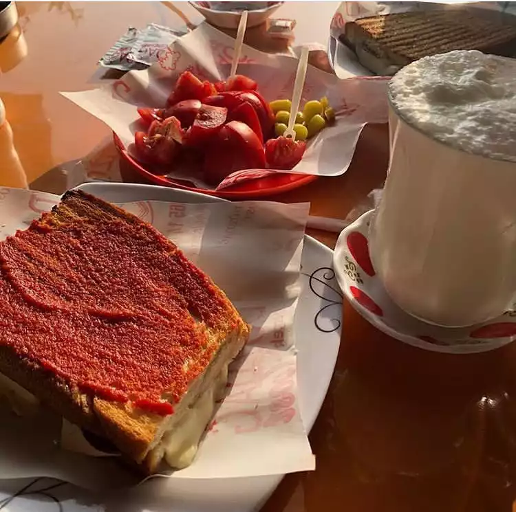 Oggusto, Salvatore Cannetiello – Şeflerin Lezzet Rotaları: Şefin favori yol üstü durağı Düzdağ Tost'ta hazırlanan, üzeri salçalı ve arası bol erimiş peynirli meşhur Susurluk tostu. Yanında köpüklü ayran, dilimlenmiş domates ve biber turşusu eşliğinde ahşap masada iştah açıcı şekilde sunuluyor.
