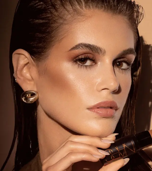 Bronz, ışıltılı ve ıslak görünümlü cildi, hafif buğulu göz makyajı ve doğal dudaklarıyla Aussie Girl Estetiğini başarıyla yansıtan modelin, elinde Nars markalı bir ürün tuttuğu bu görsel, zahmetsiz bronzluk trendinin pürüzsüz ve canlı bir örneğini sunuyor.