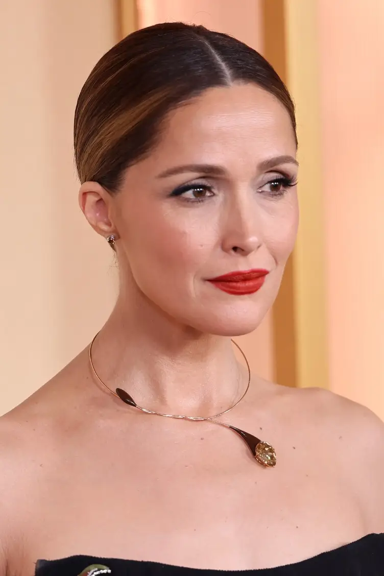 2026 Oscar ödülleri törenindeki şıklığıyla dikkat çeken Rose Byrne, bu yakın çekim portresinde geriye taranmış saçları, parlak kırmızı ruju ve zarif duruşuyla göz kamaştırırken, boynundaki özgün tasarımlı altın rengi kolyesiyle kırmızı halı stilini tamamlıyor.