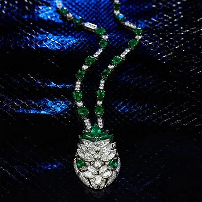 Koyu, ışıltılı bir zeminde sergilenen bu Serpenti Seduttori kolye, platin üzerine özenle işlenmiş parlak elmaslar ve canlı yeşil zümrüt taşlarıyla bezenmiş, merkezinde karmaşık bir motif oluşturan göz alıcı ve lüks bir tasarıma sahiptir.