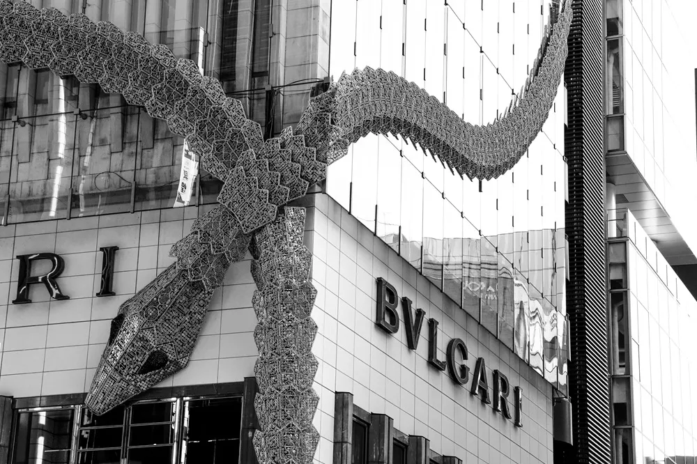 Tokyo'daki Bulgari mağazasının cephesini süsleyen, binanın etrafına dolanmış, detaylı işlemeli ve pullu bir yılan heykeli, markanın ikonik tasarımlarını yansıtarak etkileyici bir mimari detay sunuyor.