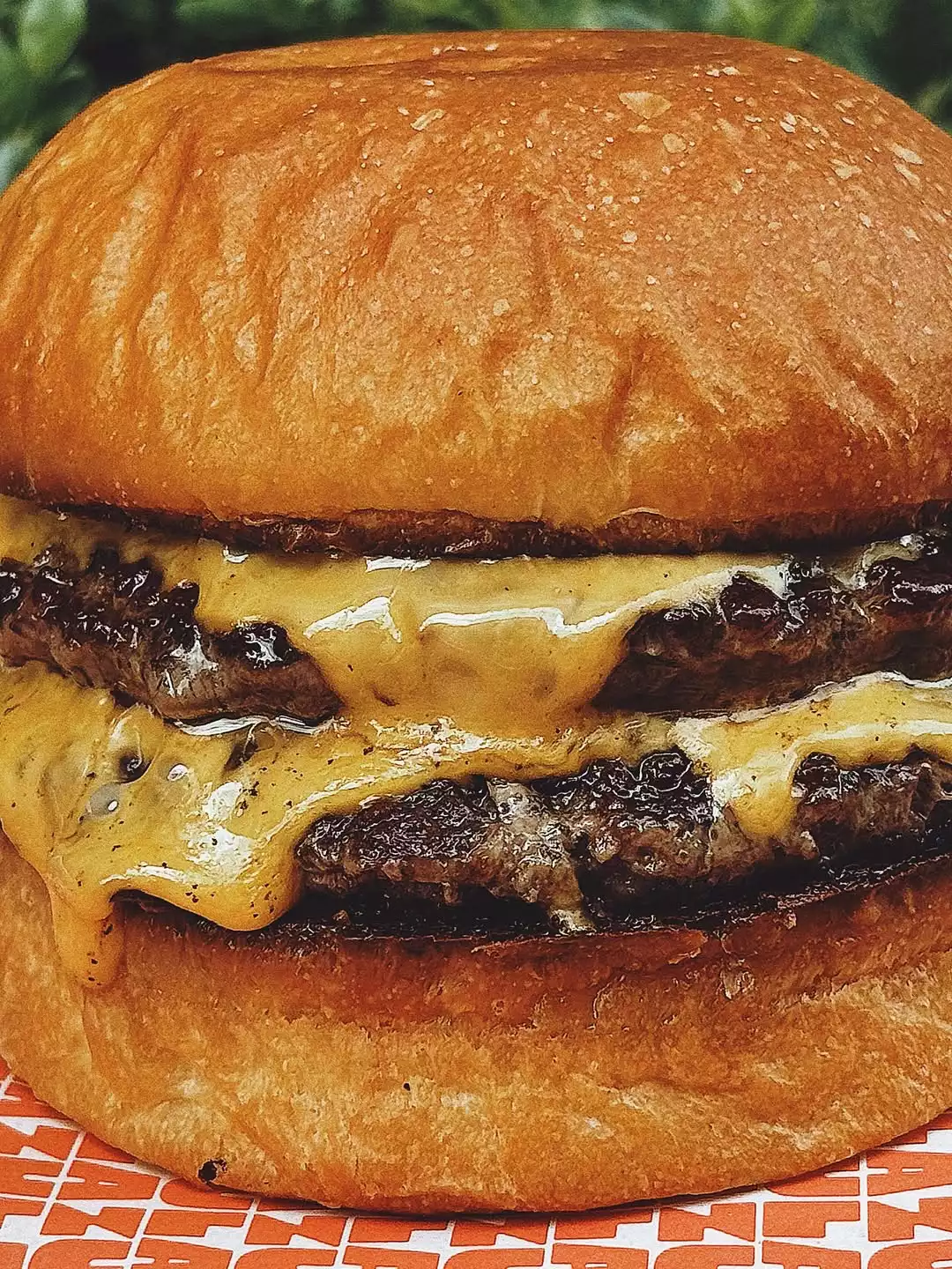 Oggusto Salvatore Cannetiello – Şeflerin Lezzet Rotaları içeriğinde şefin favori mekanı Zula'yı temsil eden çift köfteli cheeseburger. Parlak brioche ekmeği arasında, kenarlarından erimiş peynir süzülen iki kalın köfte, turuncu beyaz desenli sarma kağıdı üzerinde iştah açıcı duruyor.