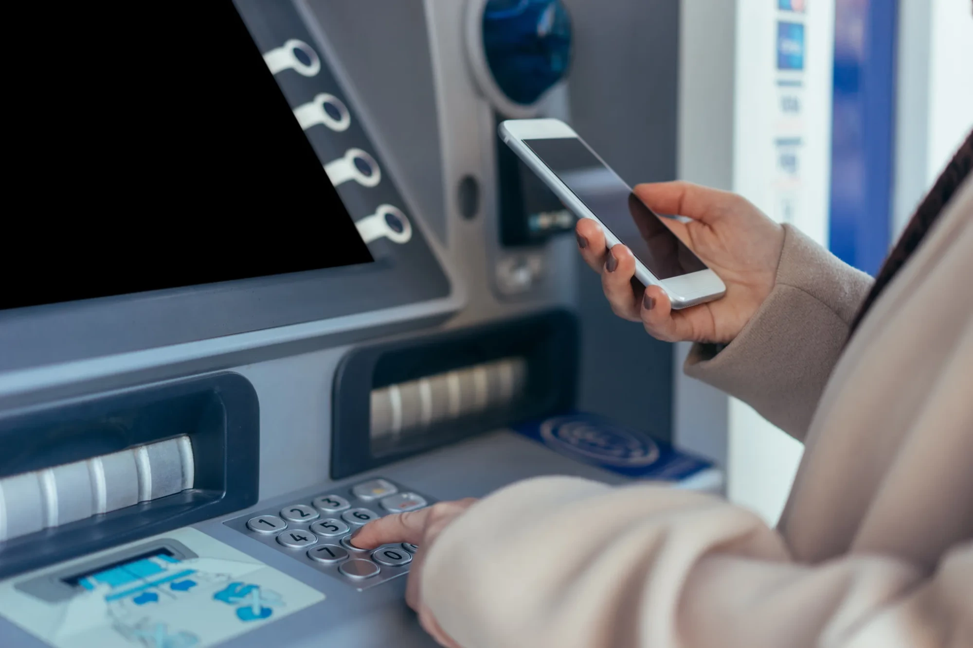 ATM'de tuş takımına basan ve akıllı telefon tutan bir kişinin yakın plan görüntüsü, Nisan ayında Aslan burcunun finansal durumunda beklenen kazançları ve sürpriz artışları temsil ediyor.