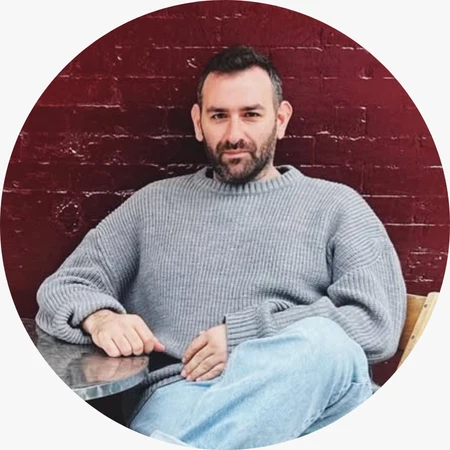 Aykun Taşdöner, sade ve rahat bir stilin öne çıktığı bu portrede gri örgü kazak ve denim pantolon kombinasyonuyla modern, günlük bir görünüm sergiliyor. Arka plandaki kırmızı tuğla duvar ise fotoğrafa güçlü bir kontrast ve şehirli bir atmosfer katıyor.