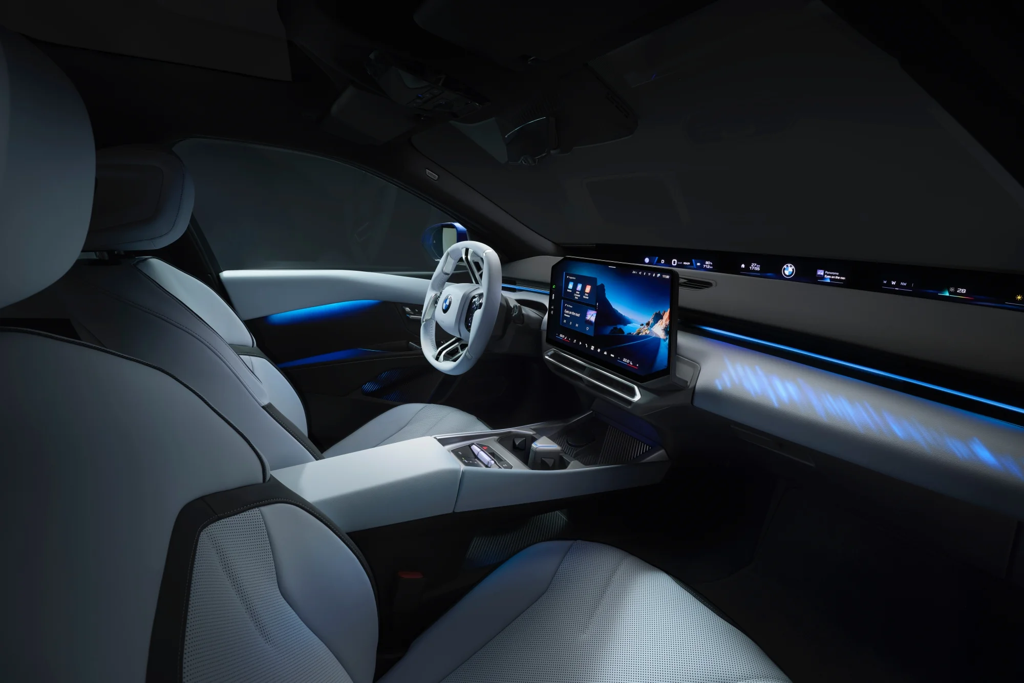 Modern bir BMW Neue Klasse i3 modelinin fütüristik iç mekanında, açık renkli deri koltuklar ve konsol, mavi ambiyans aydınlatmasıyla şık bir şekilde aydınlanırken, sürücü odaklı büyük bir iDrive dokunmatik bilgi-eğlence ekranı ve ön camın altındaki uzun Panoramic Vision gösterge paneli teknolojiyi vurguluyor.