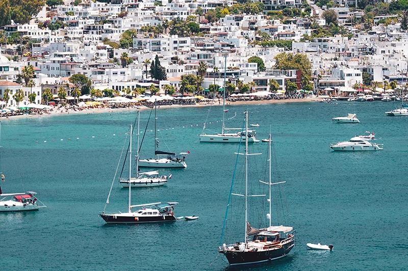 Yemyeşil tepelerle çevrili Bodrum koyunda, bembeyaz badanalı evlerin sıralandığı sahil şeridinde kalabalık bir plaj uzanırken, masmavi Ege Denizi'nde çeşitli boyutlarda birçok yelkenli ve yat huzurla süzülüyor.