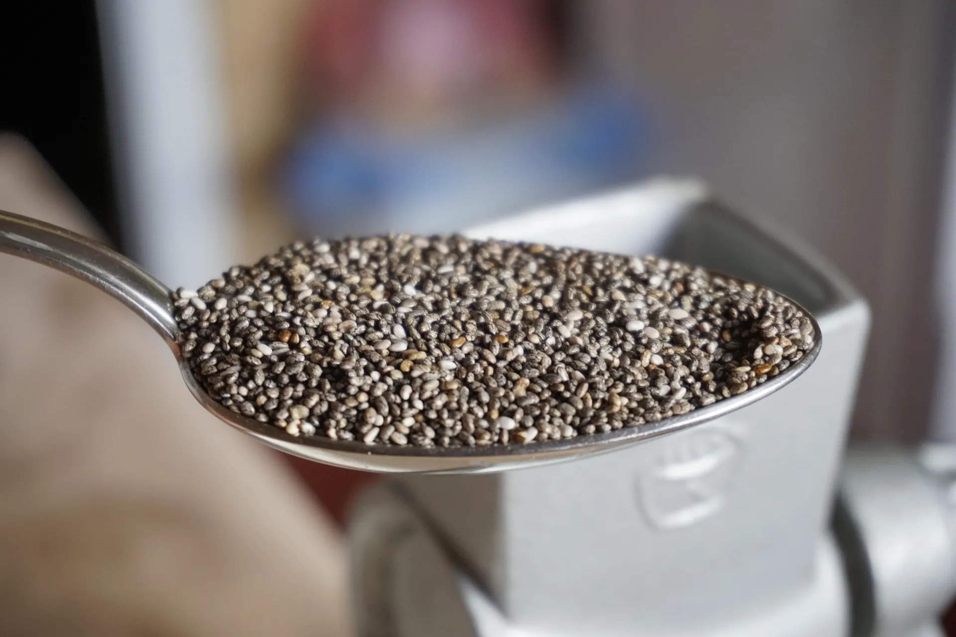 Gümüş renkli bir yemek kaşığının üzerinde, koyu gri, siyah ve açık bej tonlarında binlerce küçük ve benekli chia tohumu net bir şekilde görülüyor; bu küçük tohumlar, bilimsel kanıtlarla desteklenen sayısız faydasıyla birer besin deposu.