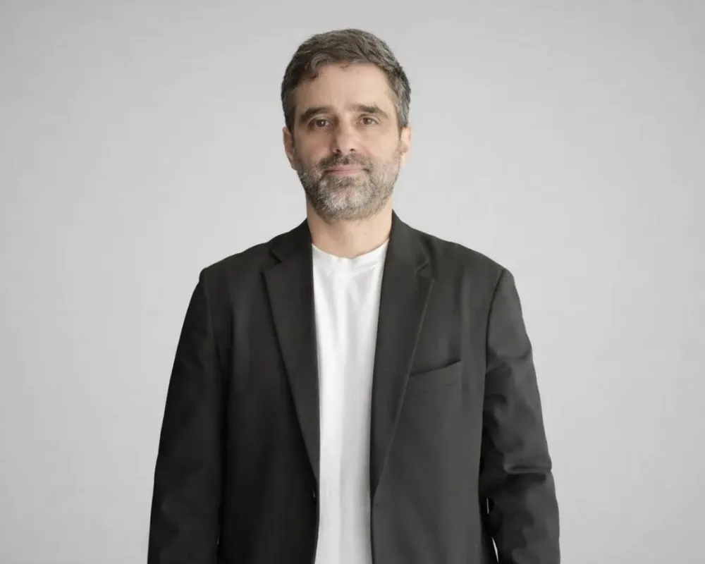 Oscar ile ilgili yazıda yer alan Deniz Yavuz'un, açık gri fon önünde, siyah ceket ve beyaz tişört giyerek doğrudan kameraya baktığı, kırlaşmış saçları ve sakalıyla samimi bir ifade taşıyan profesyonel portre fotoğrafı.