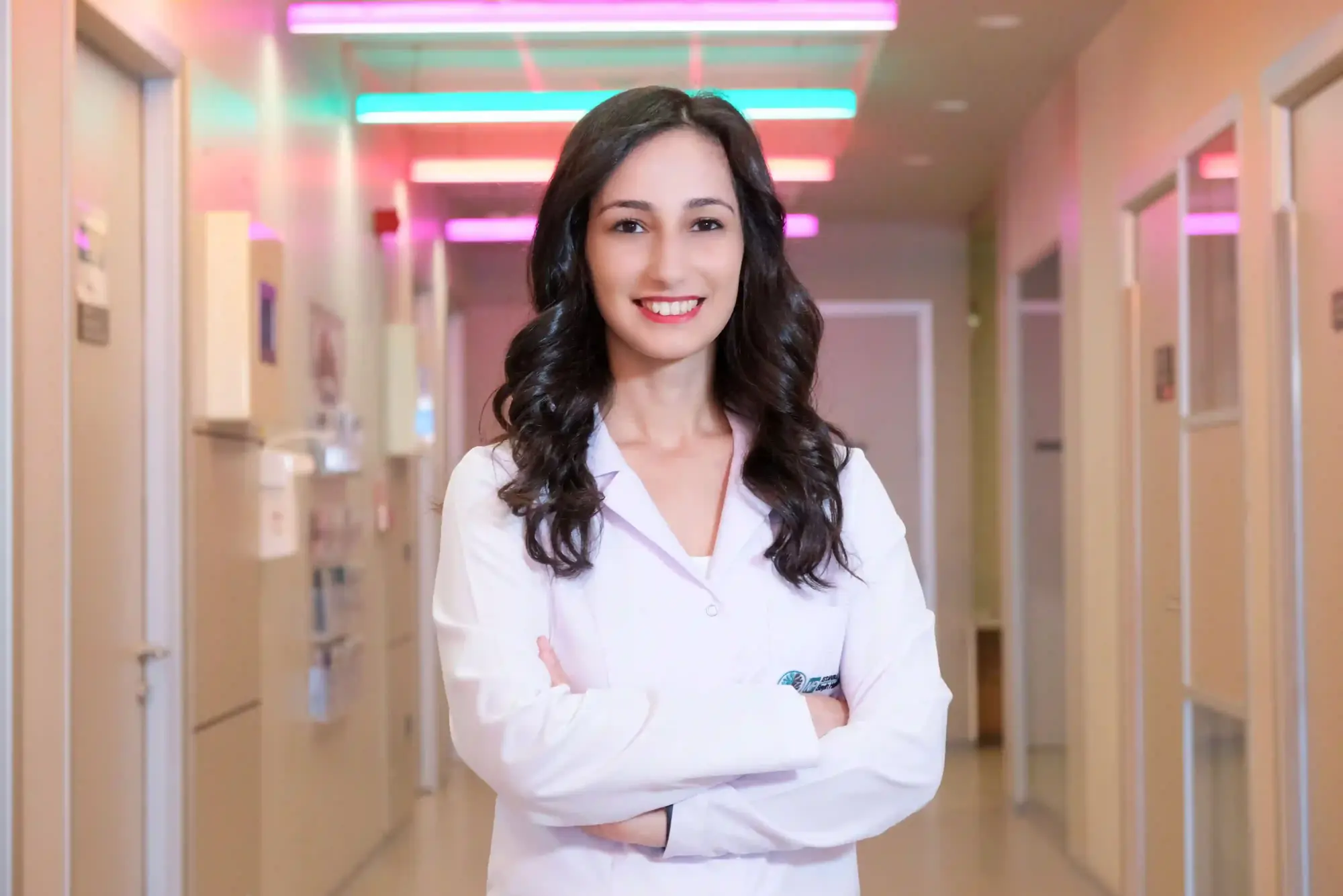 Beyaz önlüklü, kolları bağlı gülümseyen genç bir doktor, yaban mersini hakkında bilimsel bilgiler ve besin değeri üzerine rehberlik sunmak üzere modern ve renkli ışıklarla aydınlatılmış bir hastane koridorunda duruyor.