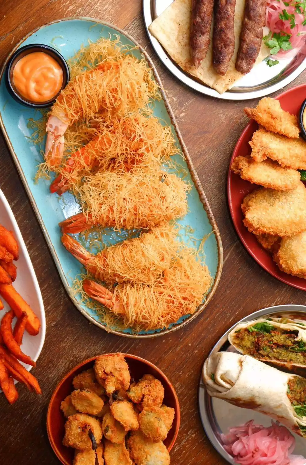 Odun bir masa üzerinde sergilenen, özellikle çıtır kadayıflı karidesler, kebaplar, kızarmış nugget'lar, tatlı patates kızartmaları ve falafel dürümler gibi çiftlikten masaya özenle hazırlanmış çeşitli ve taze ürünlerle dolu iştah açıcı bir ziyafet sofrası.