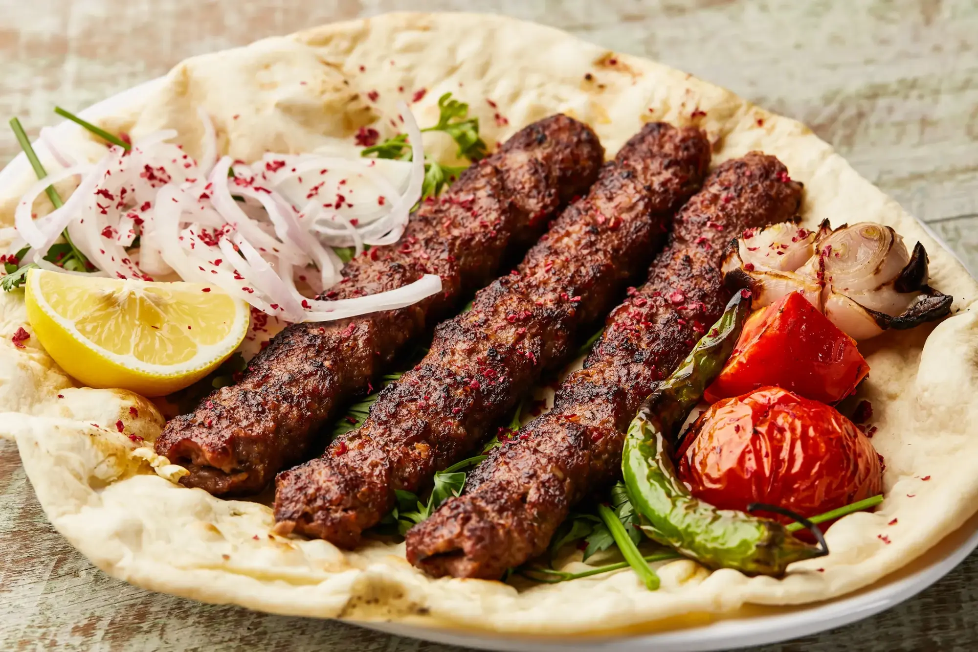 Gaziantep kebap geleneğini yansıtan, üzerinde sumaklı mor soğan, limon dilimi, közlenmiş domates ve biberlerle süslenmiş, lavaş ekmeği üzerinde servis edilen, iştah açıcı dört adet kızarmış kıyma kebap şişi.