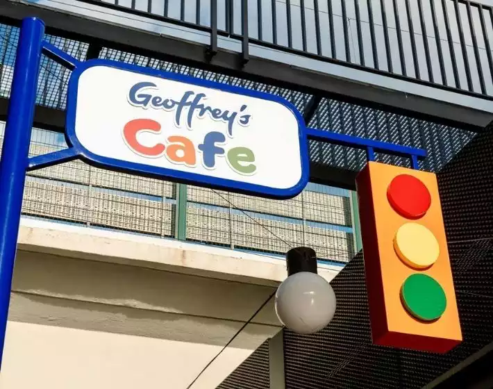 Oggusto | Terminal Kadıköy Rehberi: Lezzet, Alışveriş ve Eğlence Durakları. Modern metal mimari altındaki Geoffrey's Cafe tabelası. Mavi çerçeve içindeki renkli yazılar ve bitişiğindeki dekoratif trafik lambası, kahve molalarının eğlenceli sokak atmosferini yansıtıyor.