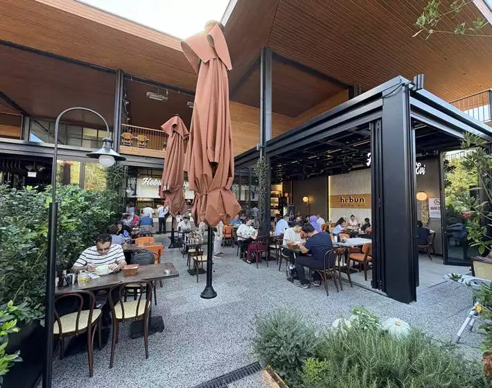 Oggusto Terminal Kadıköy Rehberi: Lezzet, Alışveriş ve Eğlence Durakları. Terminal'in popüler lezzet duraklarından Hebun Çorba Evi'nin ahşap tavanlı, yeşilliklerle çevrili açık oturma alanında yemek yiyen misafirler, alanın dinamik sokak kültürünü ve sosyalleşme ruhunu yansıtıyor.