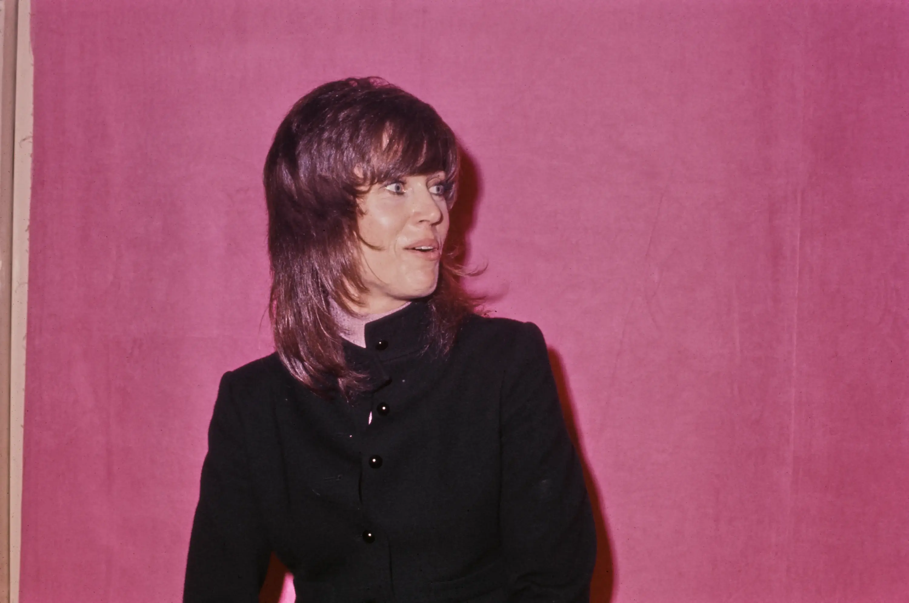 1972 Oscar Ödülleri’ne katılan Jane Fonda, yüksek yakalı siyah takım elbisesi ve dönemin karakteristik katlı saç kesimiyle sade ama güçlü bir kırmızı halı görünümü sergiliyor.