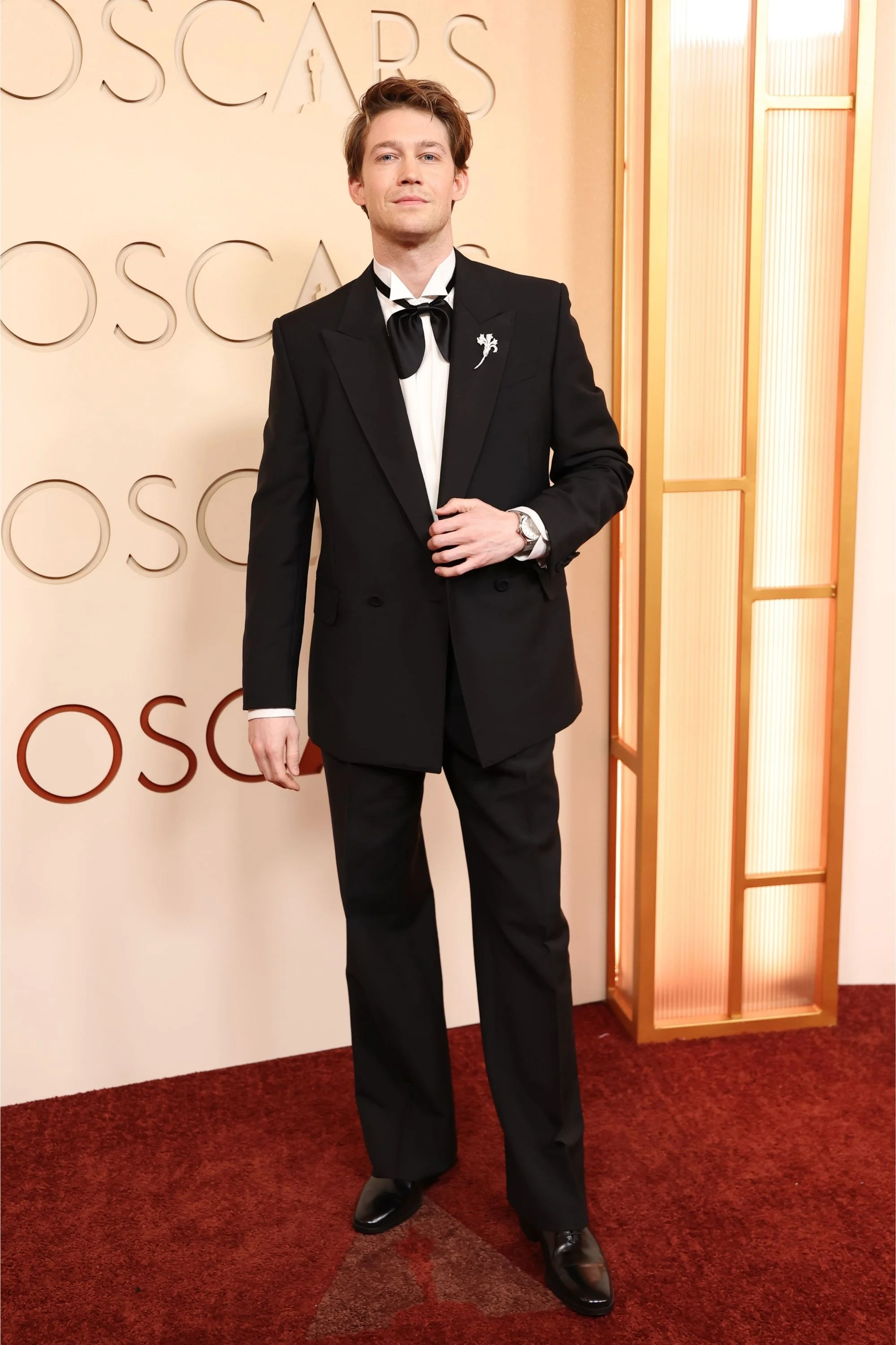 Oscar töreninde kırmızı halıda duran Joe Alwyn, şık siyah smokini, beyaz gömleği ve fiyonklu papyonuyla dikkat çekerken, sol bileğindeki Hublot Classic Fusion Essential Grey saatini zarifçe sergiliyor.