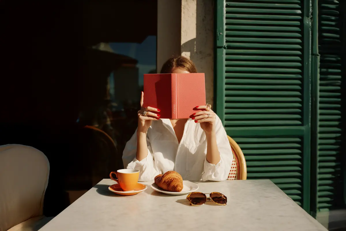 kafede kahve ve kruvasan eşliğinde kitap okuyan kadın, kitap önerileri yazısı için lifestyle kapak görseli