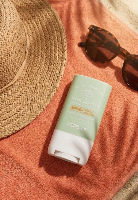 Şeftali rengi bir havlu üzerinde hasır şapka, güneş gözlüğü ve palmiye yaprağı gölgeleriyle birlikte duran Korecos Cica+Hyaluronic Acid SPF 50+ Matte Sun Stick, markaların Nisan ayındaki yeni tasarımları ve güzellik alanındaki gelişmelerini temsil ediyor.
